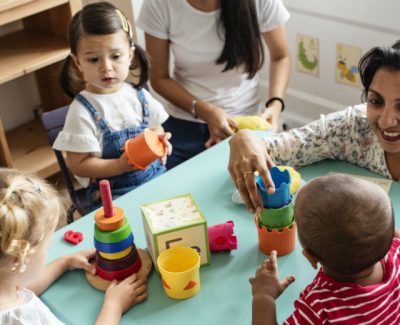 Nursery teach smiling at a play table with 3 children